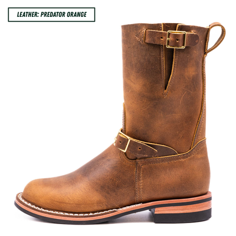 A single mid-calf leather boot in a distressed brownish-orange/cognac color, shown in profile against a white background. It features a pull tab, a decorative buckle strap, and a stacked black and tan sole.