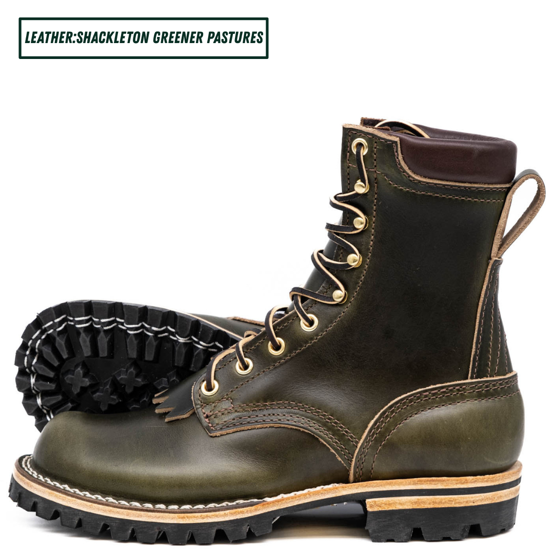 A pair of leather lace-up boots in dark olive green with gold-toned metal eyelets and a black lug sole, shown on a white background with a text label reading 'LEATHER:SHACKLETON GREENER PASTURES'.