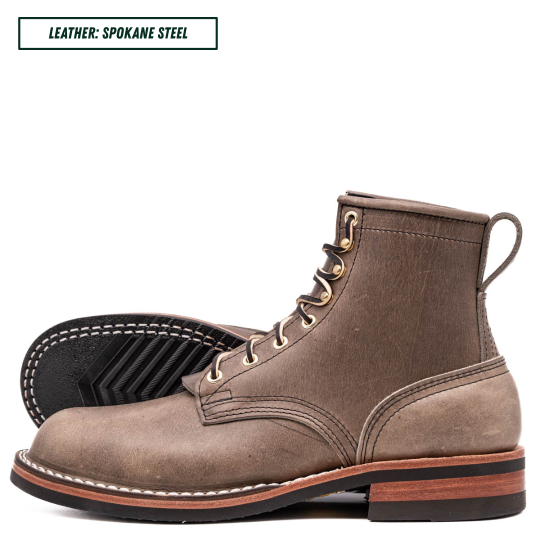 A pair of suede lace-up ankle boots in Spokane Steel brown, with one boot standing upright and the other lying on its side to show the treaded sole. A text label in the top left reads 'LEATHER: SPOKANE STEEL'.