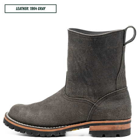 A single dark gray suede ankle boot shown in side profile on a white background, with a small text label in the top left reading 'LEATHER: 1964 GRAY'. The boot has a pull loop at the back, a rugged black lug sole, and a tan midsole layer.
