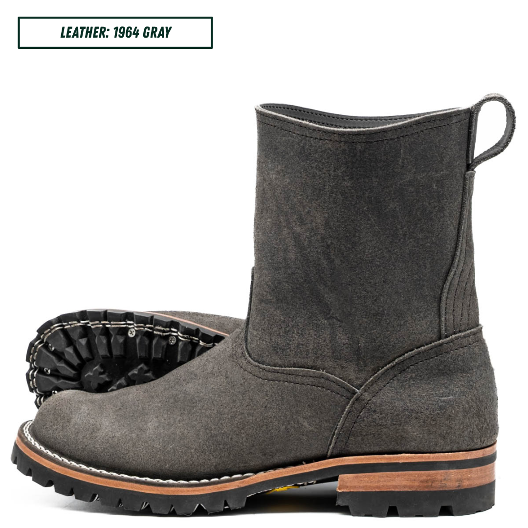 A dark gray suede ankle boot shown in side profile with a second boot placed behind it to show the sole. A text label in the top left reads 'LEATHER: 1964 GRAY'.