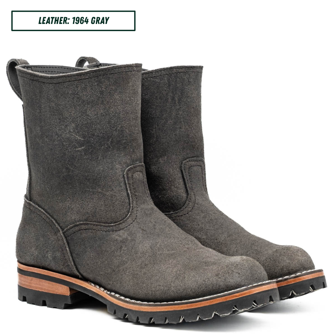 A pair of dark gray leather ankle boots with rugged lug soles and a tan midsole, shown on a white background with a text label reading 'LEATHER: 1964 GRAY'.