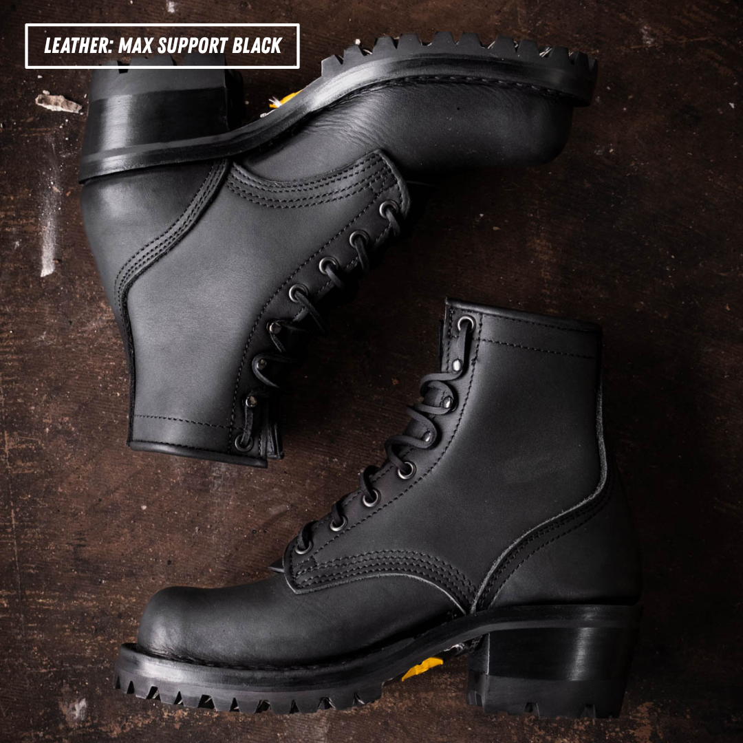 A pair of black leather lace-up ankle boots with chunky lug soles, arranged on a dark brown textured wooden surface. A text overlay in the top-left corner reads 'LEATHER: MAX SUPPORT BLACK'.