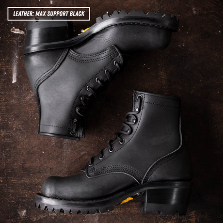 A pair of black leather lace-up ankle boots with chunky lug soles, arranged on a dark brown textured wooden surface. A text overlay in the top-left corner reads 'LEATHER: MAX SUPPORT BLACK'.