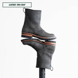 A pair of dark gray leather ankle boots stacked vertically on a display stand, with a text label in the top-left corner reading 'LEATHER: 1964 GRAY'.