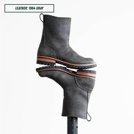 A pair of dark gray leather ankle boots stacked vertically on a display stand, with a text label in the top-left corner reading 'LEATHER: 1964 GRAY'.