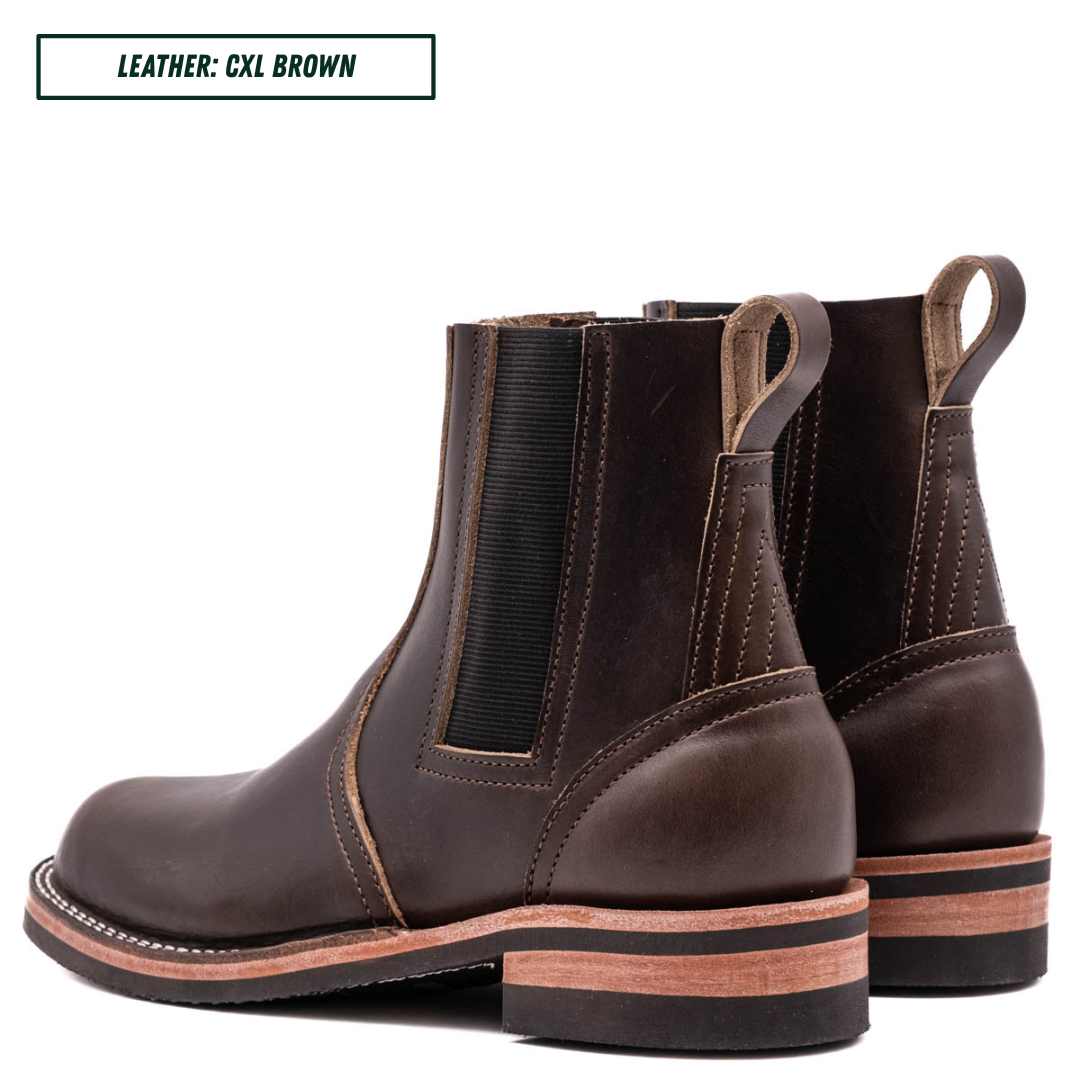 A pair of dark brown leather Chelsea boots with black elastic side panels and pull tabs, shown from a three-quarters angle on a white background. A text label in the top-left corner reads 'LEATHER: CXL BROWN'.