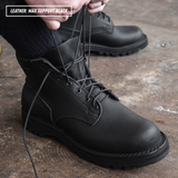 A close-up of a person wearing and tying a black leather lace-up boot, with a second matching boot blurred in the background on a rustic concrete floor. A text overlay in the top left reads 'LEATHER: MAX SUPPORT BLACK'.