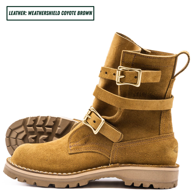 A pair of mid-calf boots in a warm coyote brown suede-like leather, featuring double buckle straps on the sides and a rugged lug sole. One boot is shown in profile while the other is turned to display the outsole.