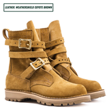 A pair of mid-calf boots in a warm coyote brown suede-like leather, featuring double buckle straps on the sides and a rugged lug sole. Boots sitting together facing forward right.