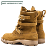 A pair of mid-calf boots in a warm coyote brown suede-like leather, featuring double buckle straps on the sides and a rugged lug sole. Boots sitting together facing back left.
