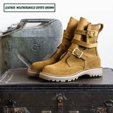 A pair of mid-calf boots in a warm coyote brown suede-like leather, featuring double buckle straps on the sides and a rugged lug sole. Boots sitting on suitcase.
