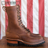 A single brown leather lace-up work boot with a chunky lug sole and stacked wooden heel, displayed on a wooden surface in front of a red and white striped flag. A text overlay in the top left reads 'LEATHER: 1964 BROWN'.