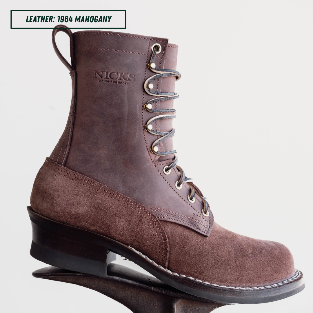 A brown suede and leather lace-up work boot by Nick's Handmade Goods, shown from a side profile on a reflective surface against a light gray background. A text label in the top left corner reads 'LEATHER: 1964 MAHOGANY'.