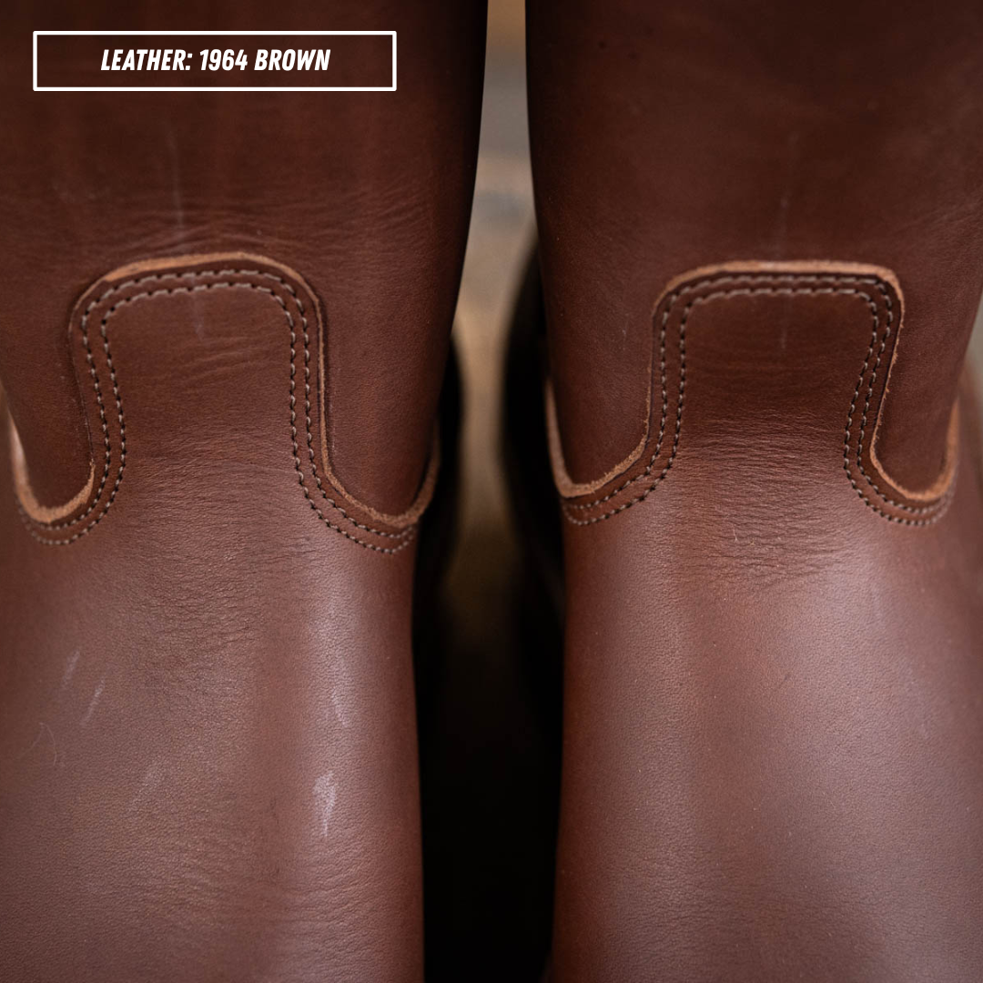 Close-up of a pair of brown leather boots showing the back of the shafts with decorative stitching and a text label in the top-left corner that reads 'LEATHER: 1964 BROWN'.
