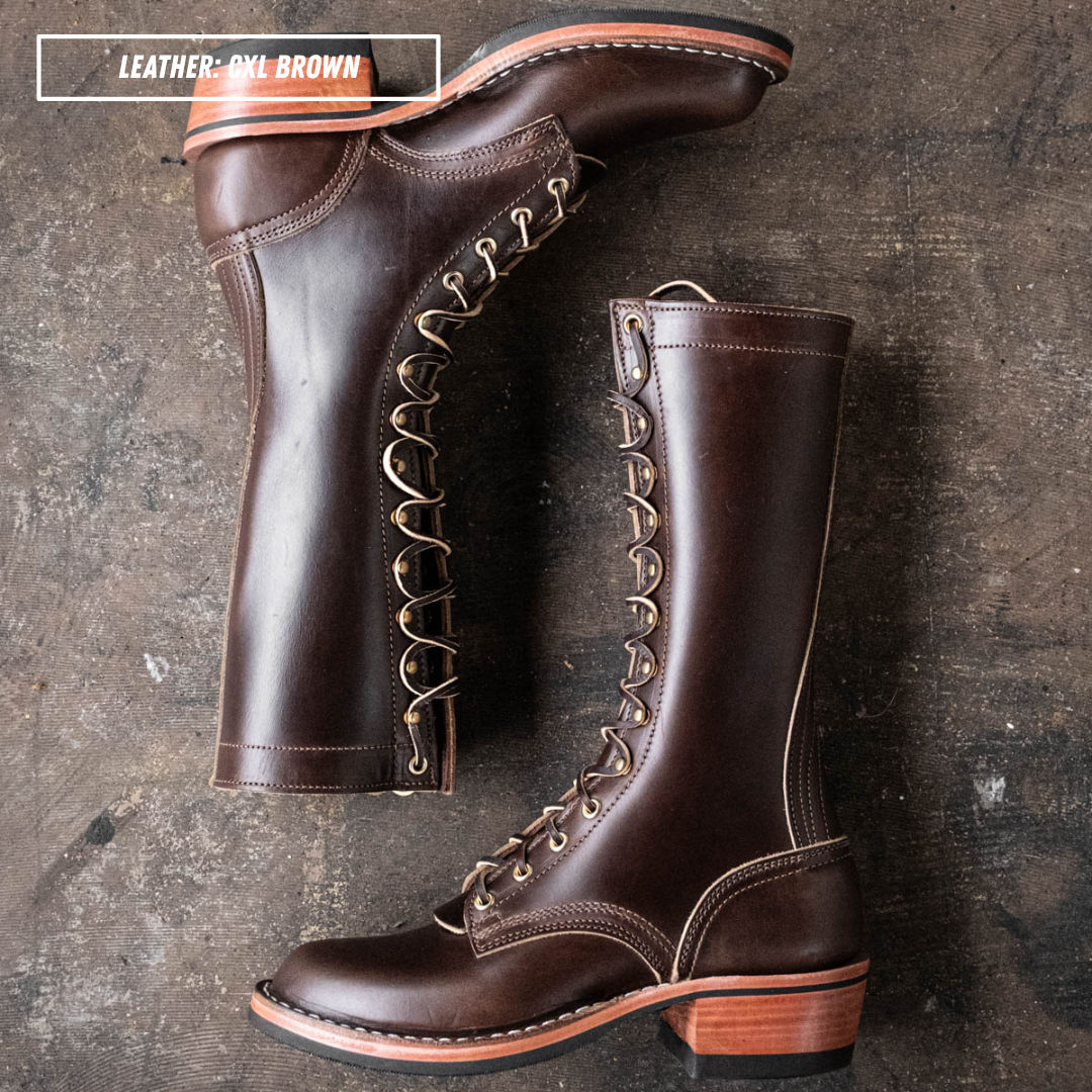 Two dark brown leather lace-up boots displayed on a textured dark surface, with one boot standing upright and the other lying on its side to show the side profile and heel.