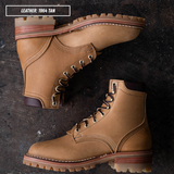 A pair of tan leather lace-up boots arranged on a dark textured surface. One boot is shown from a top-down view and the other from a side angle.