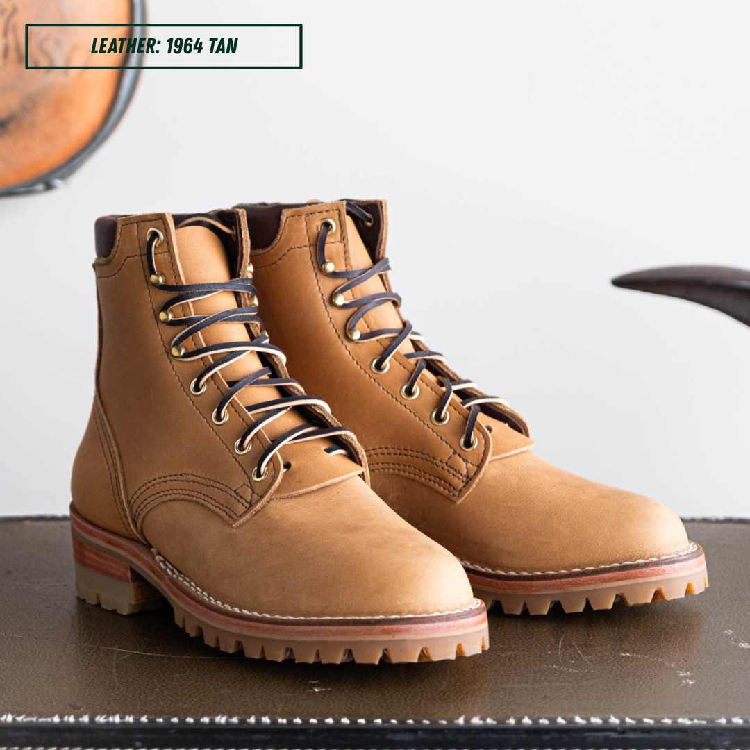 A pair of tan leather lace-up ankle boots with dark laces and metal eyelets, displayed on a dark surface against a light background. A text label in the top left reads 'LEATHER: 1964 TAN'.