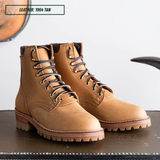 A pair of tan leather lace-up ankle boots with dark laces and metal eyelets, displayed on a dark surface against a light background. A text label in the top left reads 'LEATHER: 1964 TAN'.