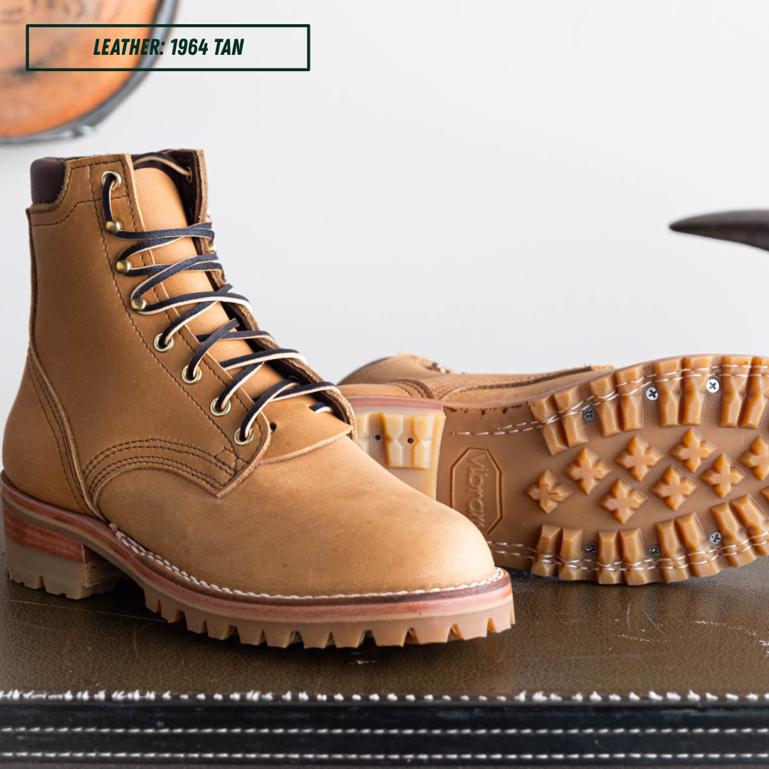 A pair of tan leather lace-up work boots, with one boot standing upright showing the side and the other lying down showing the treaded outsole. A text label in the top left reads 'LEATHER: 1964 TAN'.