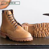 A pair of tan leather lace-up work boots, with one boot standing upright showing the side and the other lying down showing the treaded outsole. A text label in the top left reads 'LEATHER: 1964 TAN'.