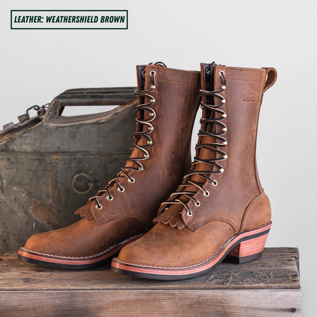 A pair of mid-calf lace-up boots in a weathered brown leather, styled on a rustic wooden surface with a vintage metal case in the background. A text overlay in the top left reads 'LEATHER: WEATHERSHIELD BROWN'.