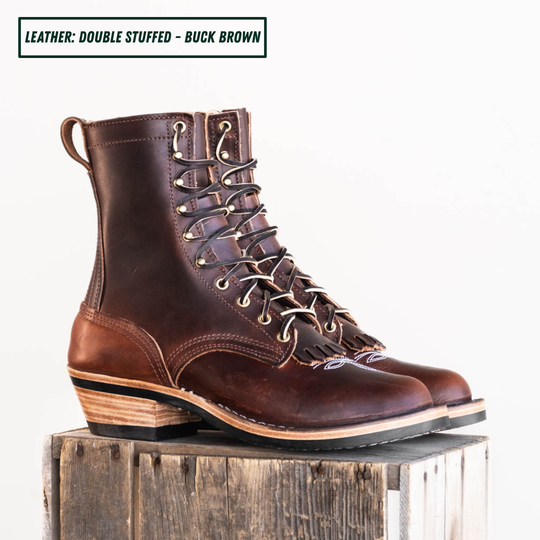 A pair of double-stuffed buck brown leather lace-up ankle boots with stacked wood-look heels, displayed on a rustic wooden block against a white background. A text overlay at the top reads 'LEATHER: DOUBLE STUFFED - BUCK BROWN'.