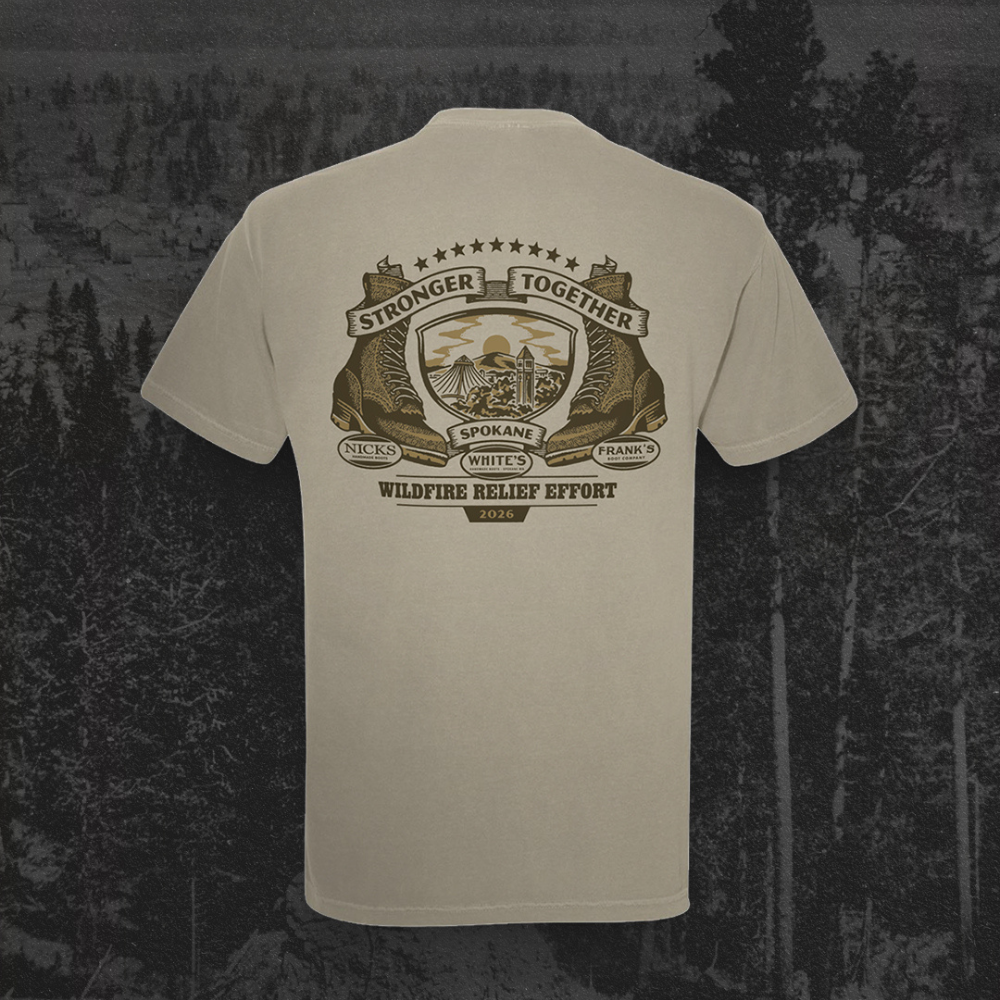 A light beige crewneck t-shirt shown from the back, featuring a large brown and gold graphic print with the text 'Stronger Together Wildfire Relief Effort' and 'Spokane County, Washington'. The shirt is displayed against a dark, moody forest background.