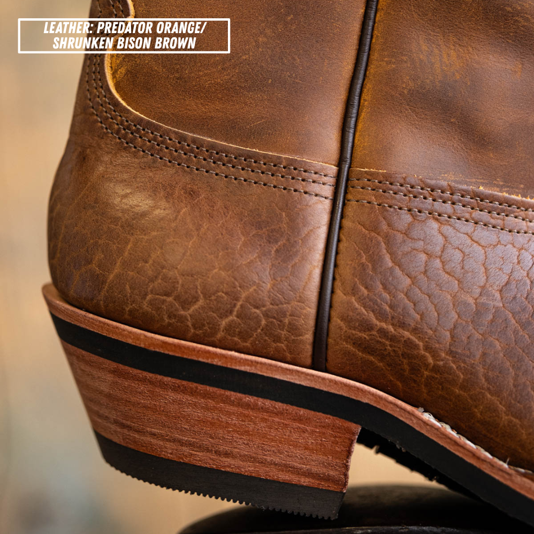 Close-up of a brown leather boot corner showing the textured leather vamp, stitching, stacked wood-look heel, and black outsole. A text box in the top left reads 'LEATHER: PREDATOR ORANGE/ SHRUNKEN BISON BROWN'.