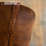 Close-up of a distressed brown leather boot with a pull tab and a text label overlay in the top left corner reading 'LEATHER: PREDATOR ORANGE/ SHRUNKEN BISON BROWN'.