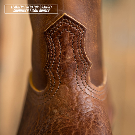 Close-up of a textured brown leather boot shaft with decorative stitching and a text label in the top-left corner reading 'LEATHER: PREDATOR ORANGE/ SHRUNKEN BISON BROWN'.