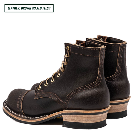 A pair of dark brown leather lace-up boots with a rugged sole and stacked heel, shown from a three-quarters angle on a white background. A text label in the top-left corner reads 'LEATHER: BROWN WAXED FLESH'.