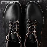 A pair of black leather lace-up boots shown from a top-down view on a dark textured surface. White contrast stitching outlines the edges, and the laces are threaded through brass eyelets.