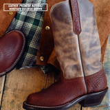 A leather cowboy boot in brown and tan distressed leather, shown alongside a matching brown leather pull tab and a green plaid shirt on a rustic wooden surface. A text overlay in the top left reads 'LEATHER: PREDATOR NATURAL / MINOTAUR BULLHIDE BROWN'.