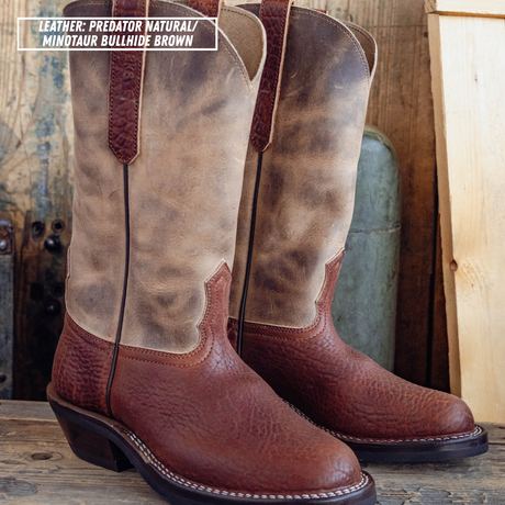 A pair of tall western boots in distressed brown leather, shown standing on a wooden surface against a rustic wood and metal background. A text label in the top left reads 'LEATHER: PREDATOR NATURAL / MINOTAUR BULLHIDE BROWN'.