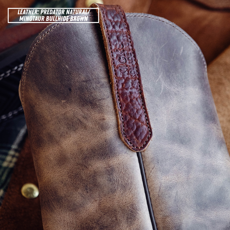 A close-up of a distressed leather boot or holster in brown, featuring a darker brown embossed leather strap with a stitched 'CB' logo. A text overlay in the top-left corner reads 'LEATHER: PREDATOR NATURAL / MINOTUR BULLHIDE BROWN'.