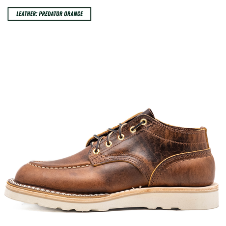 A single brown leather lace-up shoe shown in side profile on a white background, with a text label in the top-left corner reading 'LEATHER: PREDATOR ORANGE'. The shoe has a distressed medium-brown leather upper, tan stitching, light tan midsole, and off-white lug sole.