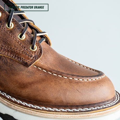 Close-up of a brown leather lace-up boot with white contrast stitching and black laces, labeled 'LEATHER - PREDATOR ORANGE' against a light gray background.