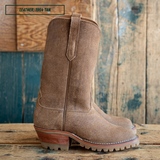 A pair of tan suede western-style boots shown in side profile on a wooden table with a wood pallet background. A small label in the top left reads 'LEATHER: 1964 TAN'.