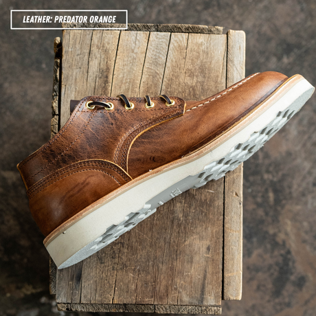 A brown leather lace-up shoe shown at an angle on a rustic wooden block, with a text label in the top-left corner reading 'LEATHER: PREDATOR ORANGE'.
