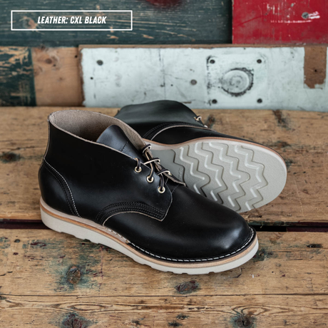 Black leather boots, one sitting up and one laying down on wooden crate. A text box in the top left corner reads 'LEATHER: CXL BLACK'.