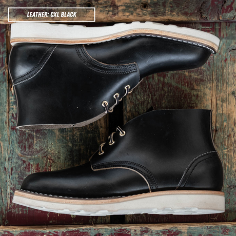 Black leather boots sitting side profile on wooden crate. A text box in the top left corner reads 'LEATHER: CXL BLACK'.