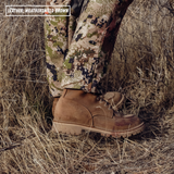 A person standing in dry grass outdoors, wearing camouflage pants and a tan leather lace-up boot. A text overlay in the top left reads 'LEATHER: WEATHERSHIELD BROWN'.