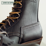 Close-up of a dark brown leather lace-up boot with tan laces and visible stitching, showing the side heel and part of the collar. A small text overlay in the top left reads 'LEATHER: MAX SUPPORT BOOT.