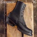 A black leather boot laying on wooden crate. Label on top left reads 'LEATHER: MAX SUPPORT BLACK'