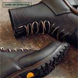 Close-up of a pair of black leather lace-up boots on a rustic brown textured surface. One boot is angled to show the side profile with metal eyelets and laces.