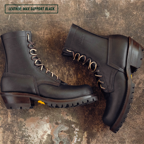 A pair of black leather lace-up boots arranged on a distressed brown textured surface. One boot is shown in profile with its laces threaded through metal eyelets, and the other is angled to show the side and heel.