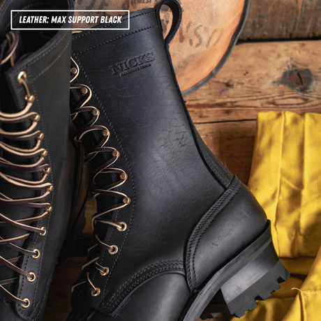 A close-up of a black leather lace-up boot with metal eyelets, shown alongside another boot and a yellow cloth on a rustic wooden surface. Text in the top-left corner reads 'LEATHER: MAX SUPPORT BLACK' and the embossed brand 'NICKS' is visible on the side of the boot.