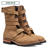 A pair of mid-calf leather boots in tan leather with multiple wrap-around straps and brass-tone buckles, shown on a white background with a small label reading 'LEATHER: 1964 TAN'.