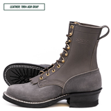A pair of gray suede lace-up boots with gold-tone eyelets and white contrast stitching, shown on a white background with one boot standing upright and the other lying on its side to display the sole. A text label in the top left reads 'LEATHER: 1964 ASH GRAY'.